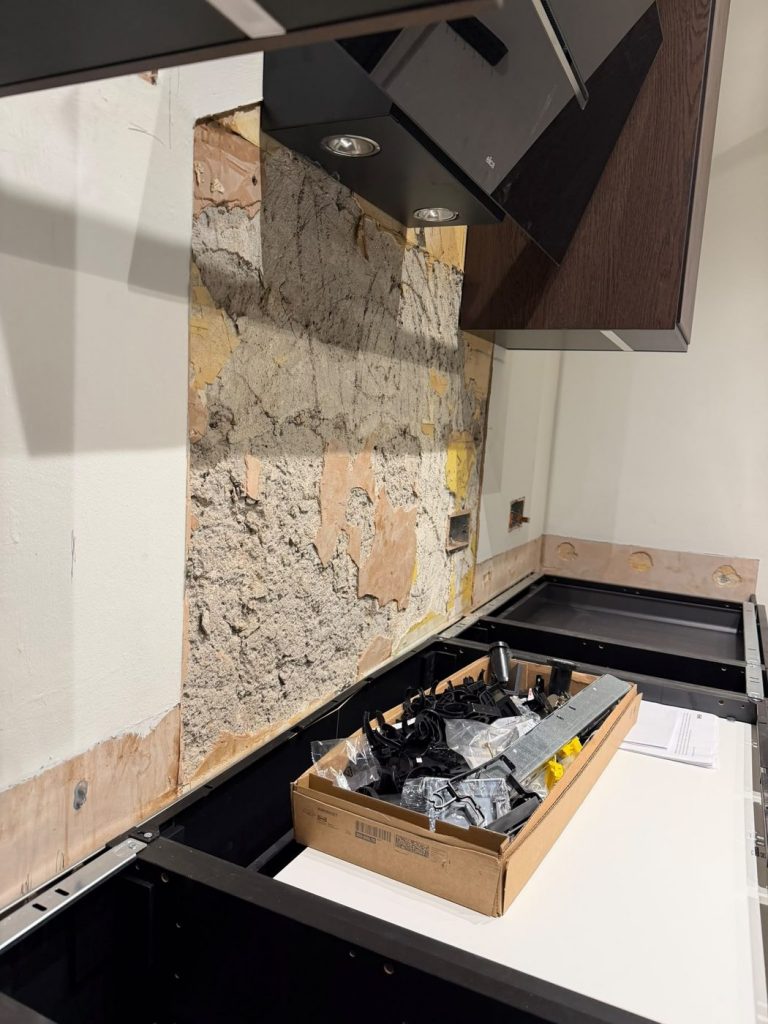 Dry-fitted IKEA base units with no worktop and a patched, uneven wall above