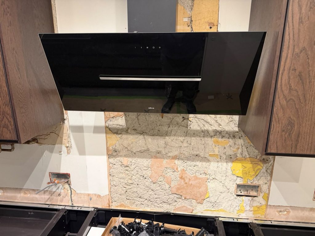 IKEA kitchen dry fit with old tiles stripped from the wall behind the hob, leaving rough uneven plaster