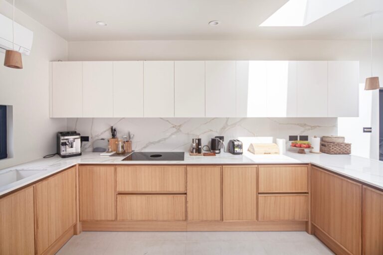 U-shaped oak and white handleless kitchen under a skylight