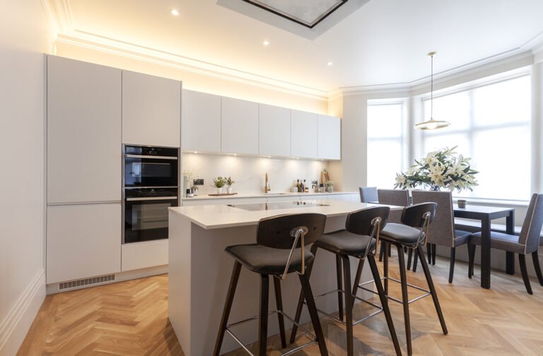 Kitchen island with bar stools and built-in ovens in a bay-windowed Hampstead kitchen