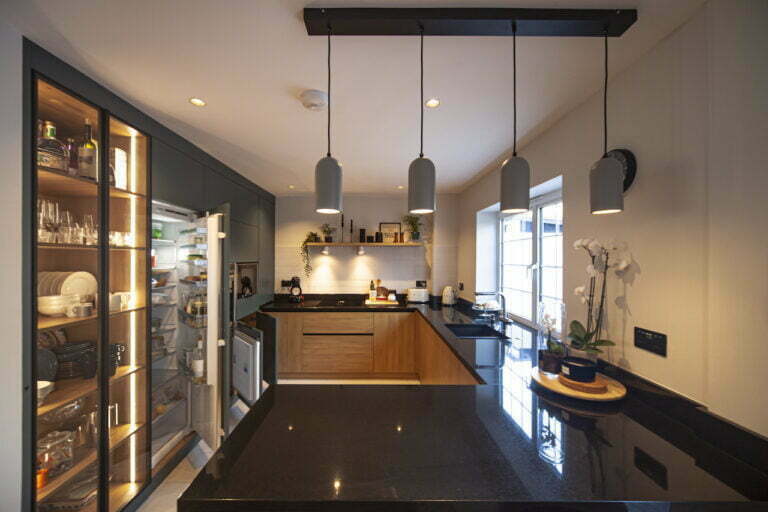 Open-plan kitchen with black worktop island, pendant lights and glass display cabinet